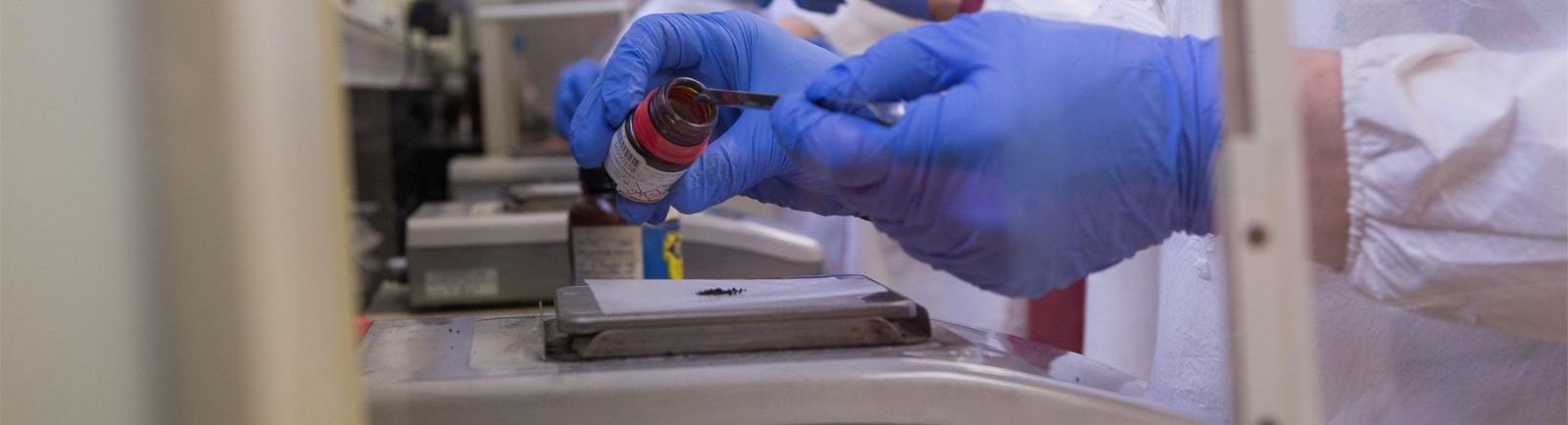 亿德体育化学系的学生在实验室里戴着手套从罐子里取出材料.