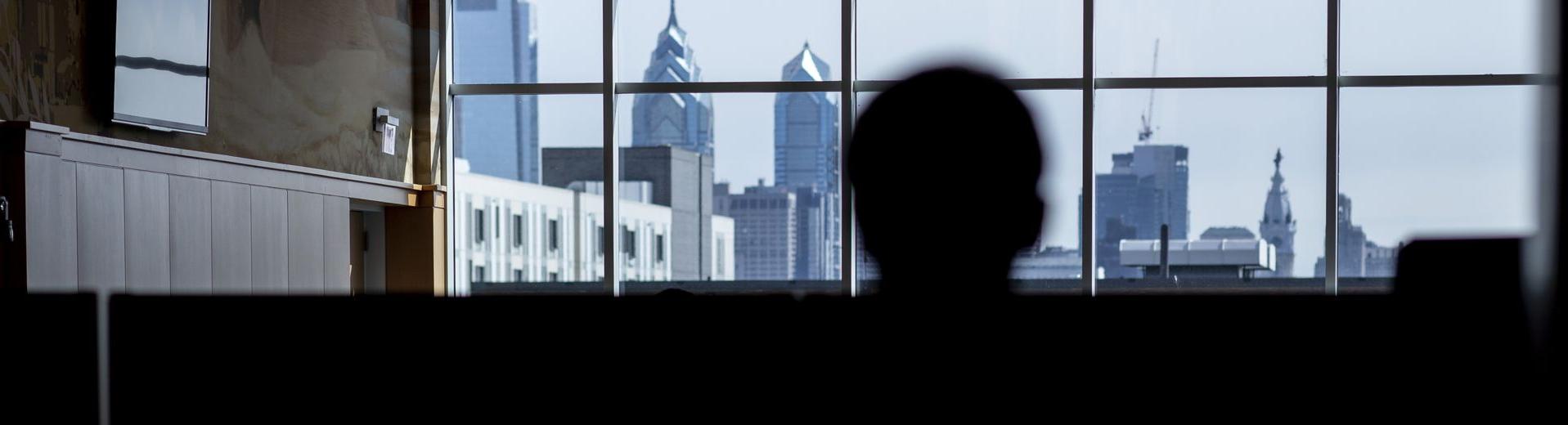 A student looks at the Philadelphia skyline through the windows of a building at Temple University.
